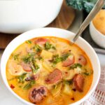 A white bowl with a spoon in it, filled with Sausage, Kale And Potato Soup.