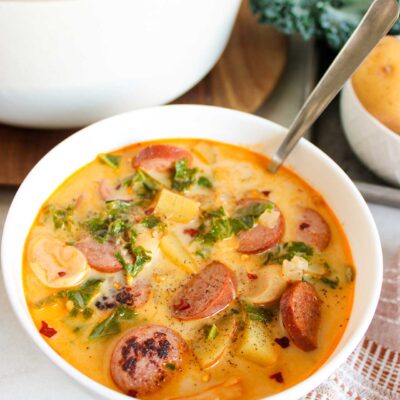 A white bowl with a spoon in it, filled with Sausage, Kale And Potato Soup.