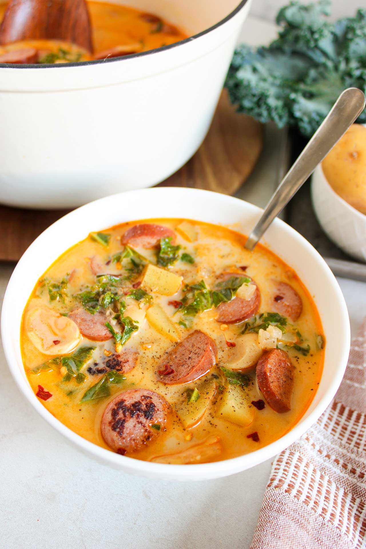 A white bowl with a spoon in it, filled with Sausage, Kale And Potato Soup.