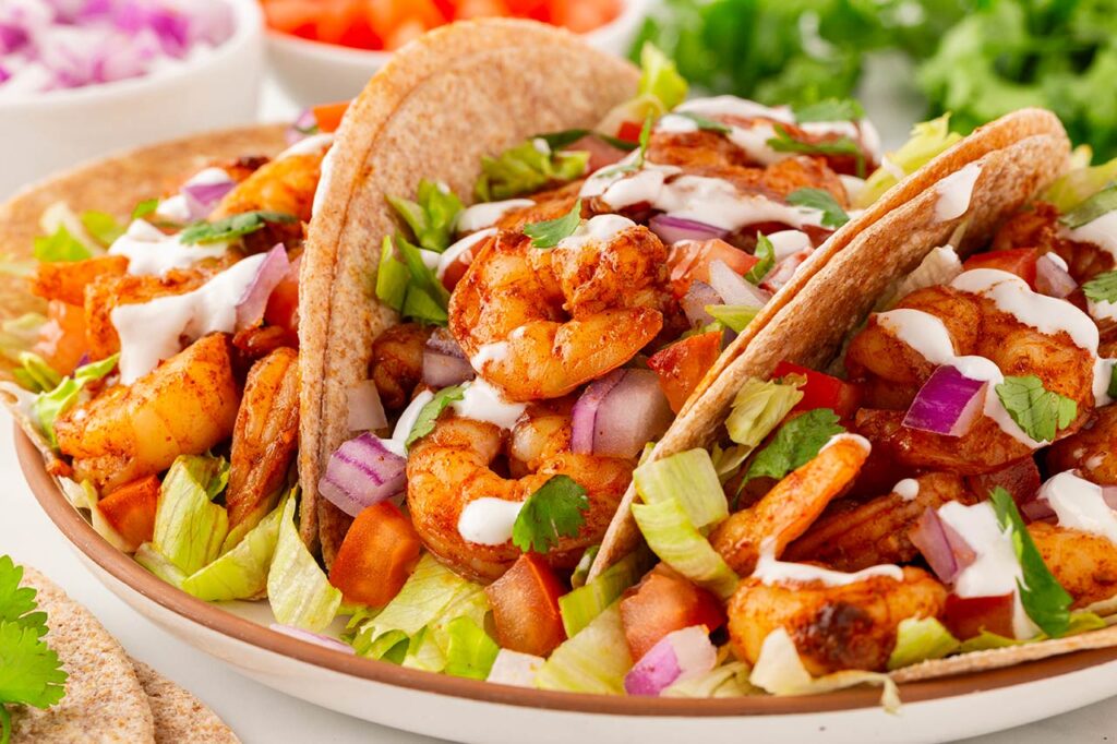 Side view of three shrimp tacos lined up on a white platter.