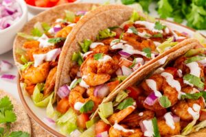 Side angled view of three shrimp tacos on a white platter.