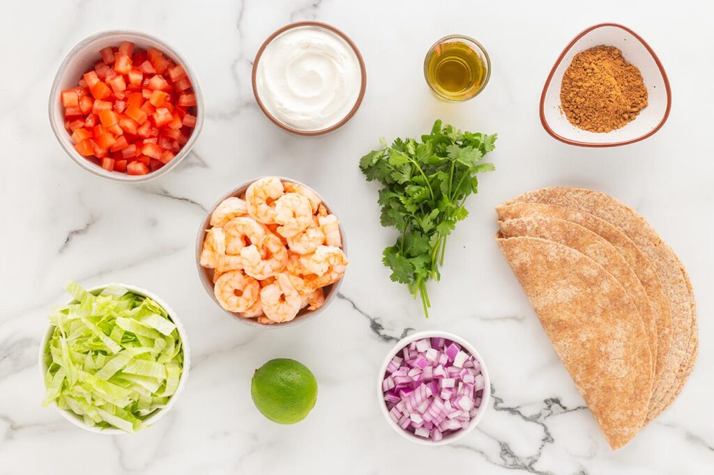 Ingredients for shrimp tacos on a white, marble surface.