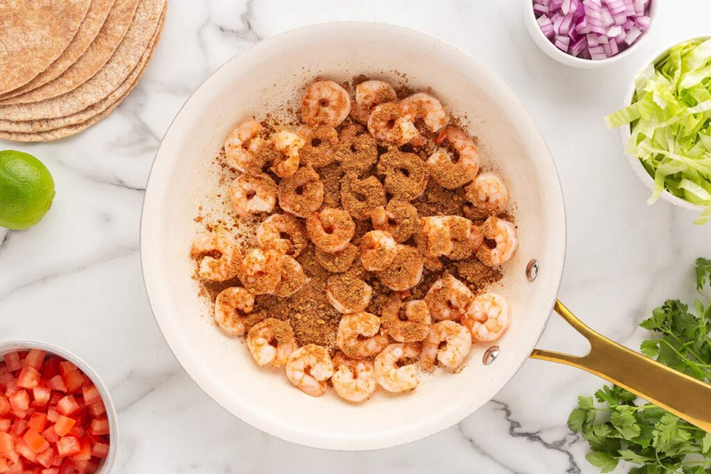 Spices added to shrimp in a skillet.