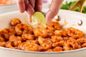 Squeezing fresh lime juice over cooked shrimp in a skillet.