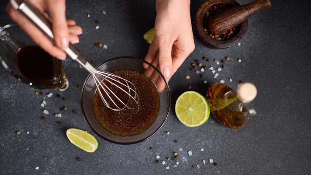 Woman mixing teriyaki sauce with whisk in a glass bowl.