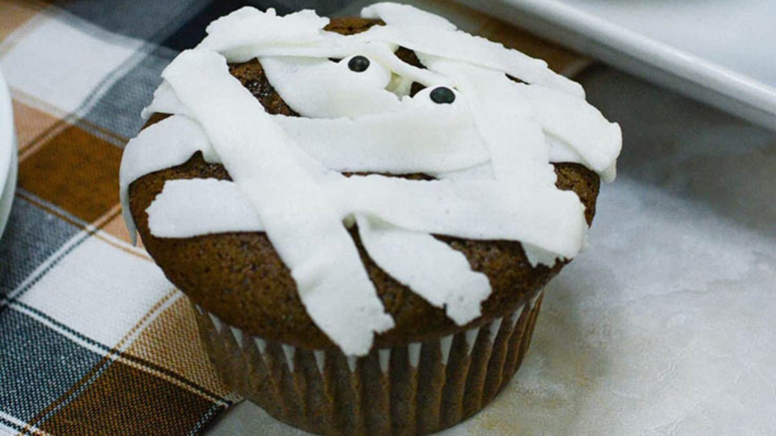 A single chocolate cupcake with white mummy frosting and googly eyes on top.