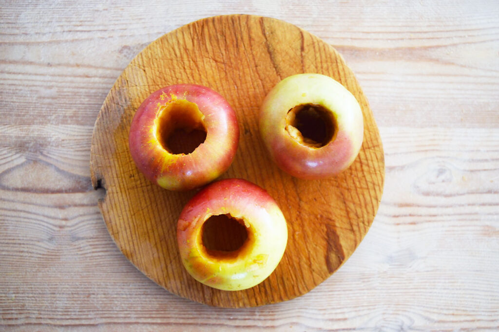Three cored apples on a cutting board.