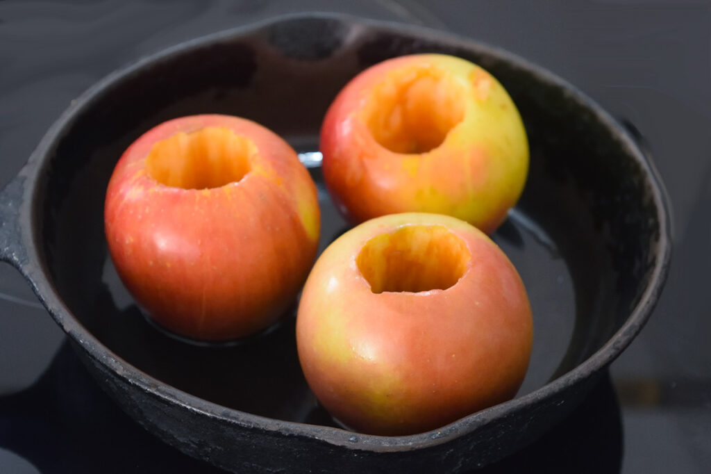 Three cored apples in an oiled cast iron skillet.