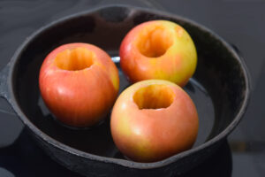 Three cored apples in an oiled cast iron skillet.