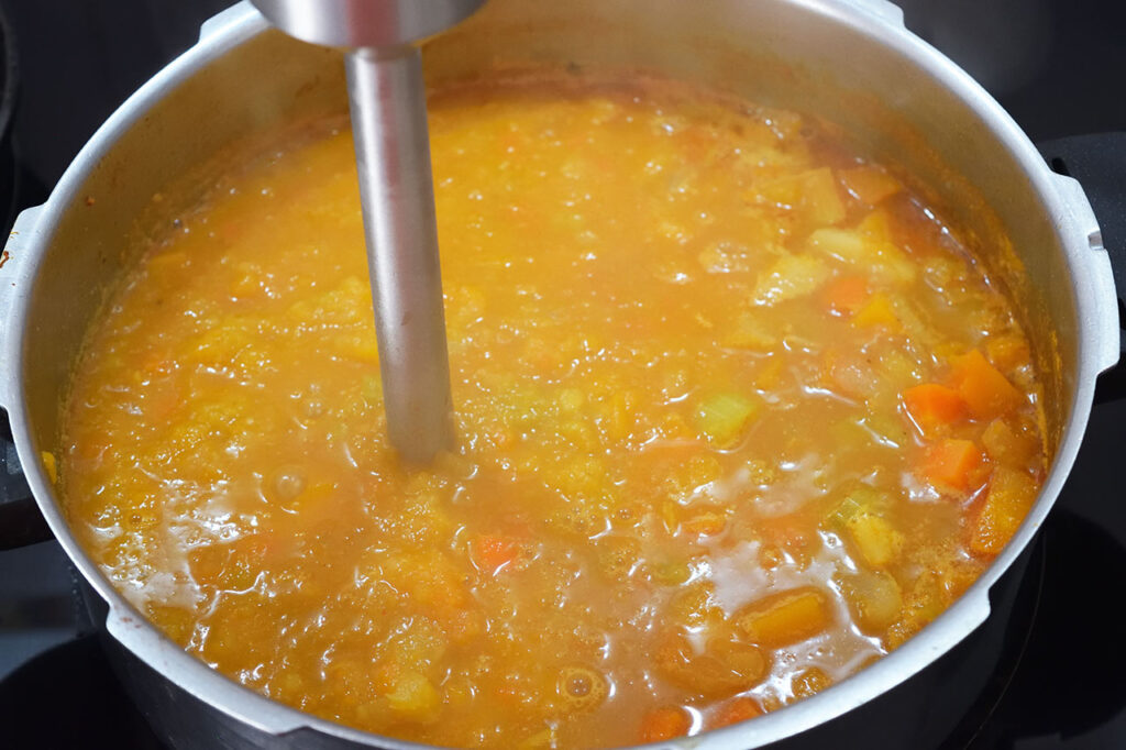 Using a stick blender to blend soup in a pot.