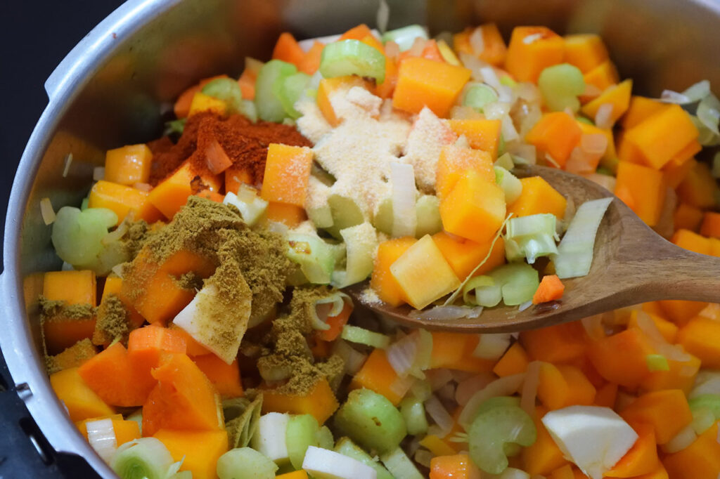 Spices added to Butternut Squash Soup vegetables in a pot.