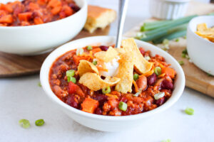 Front view of a bowl filled with Classic Chicken Chili and topped with sour cream and corn chips.