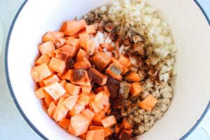 Sweet potatoes, onions spices and browned ground chicken added to a pot.
