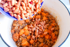 Adding beans to the chili in a pot as it cooks.