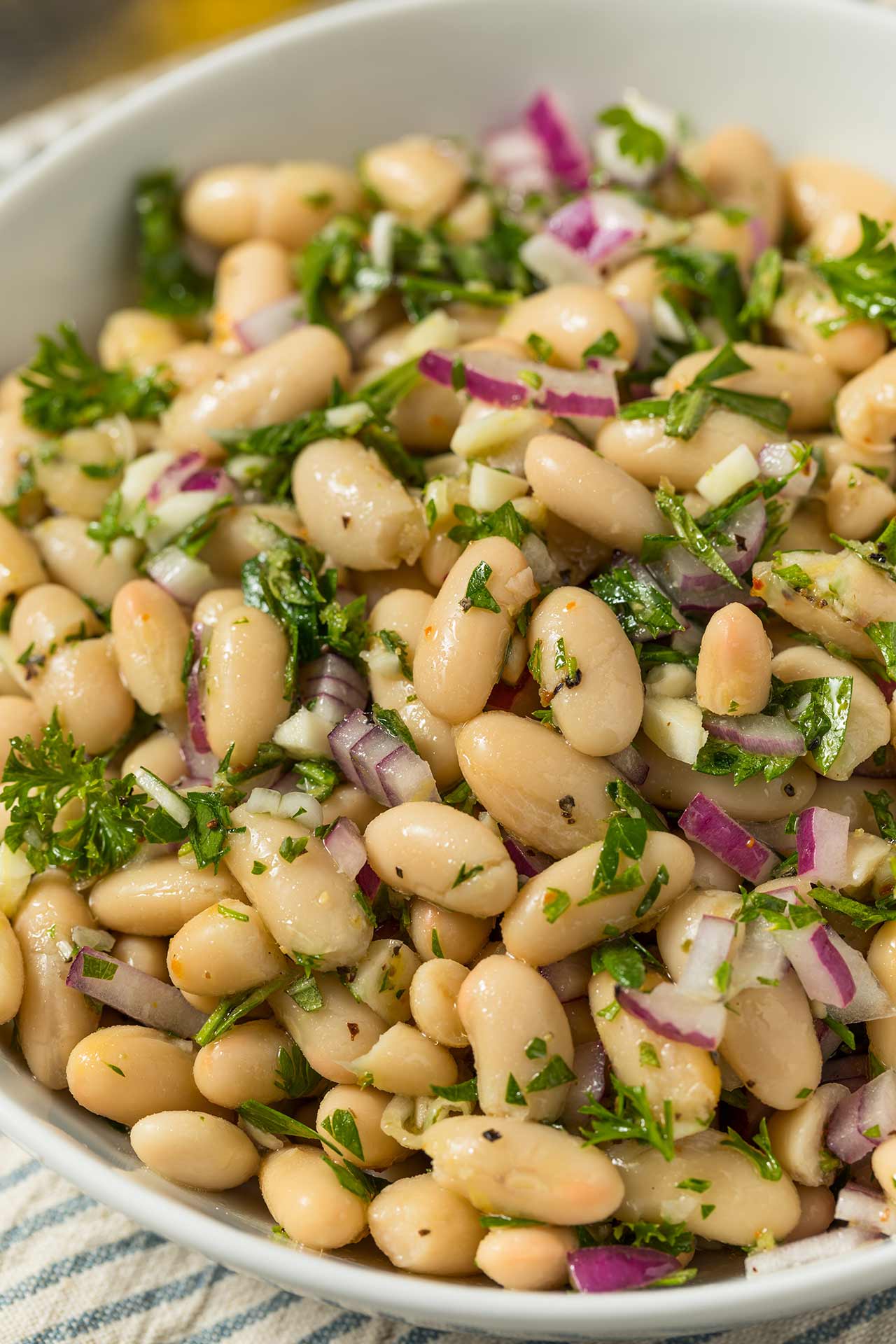 A white bean, dense bean salad in a white bowl.