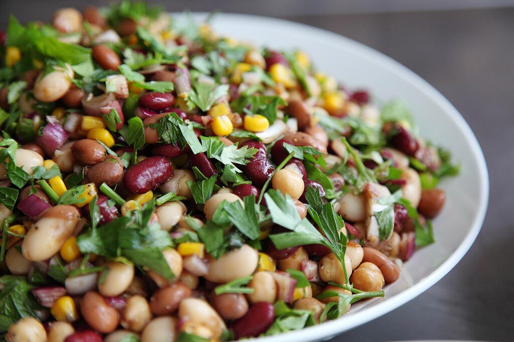 Side view of a dense bean salad with fresh herbs in a white bowl.