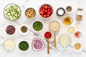 Greek Rice Bowl ingredients in individual bowls on a white marble surface.