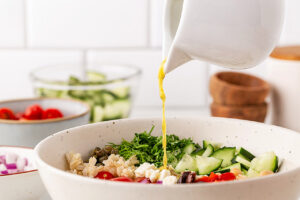 Pouring dressing over an assembled Greek Rice Bowl.