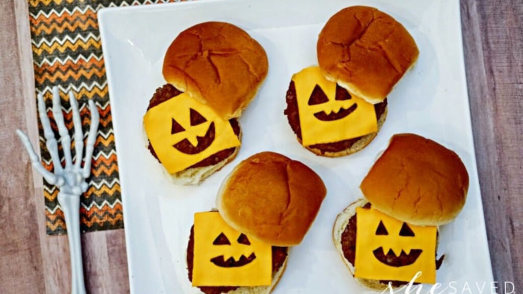 Slider burgers on a platter with slices of cheese with faces cut into them.