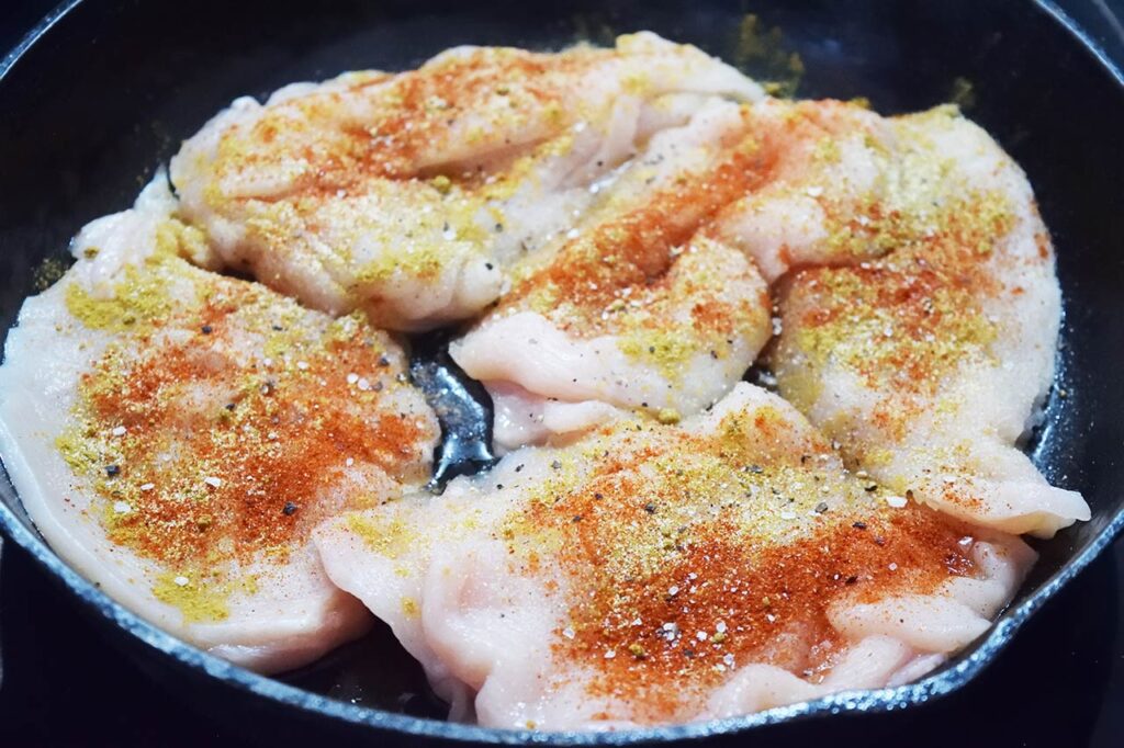 Seasoned chicken breasts in a cast iron skillet.