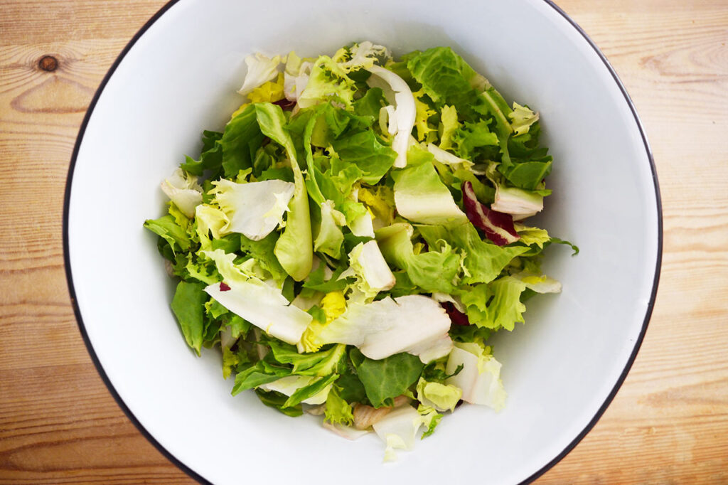 Lettuce in the bottom of a white mixing bowl.