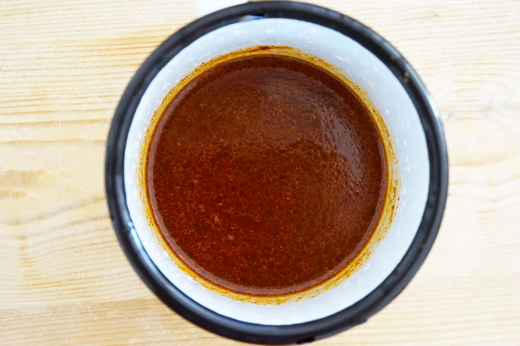 Mexican Dense Bean Salad dressing ingredients mixed together in a white cup with a black rim.