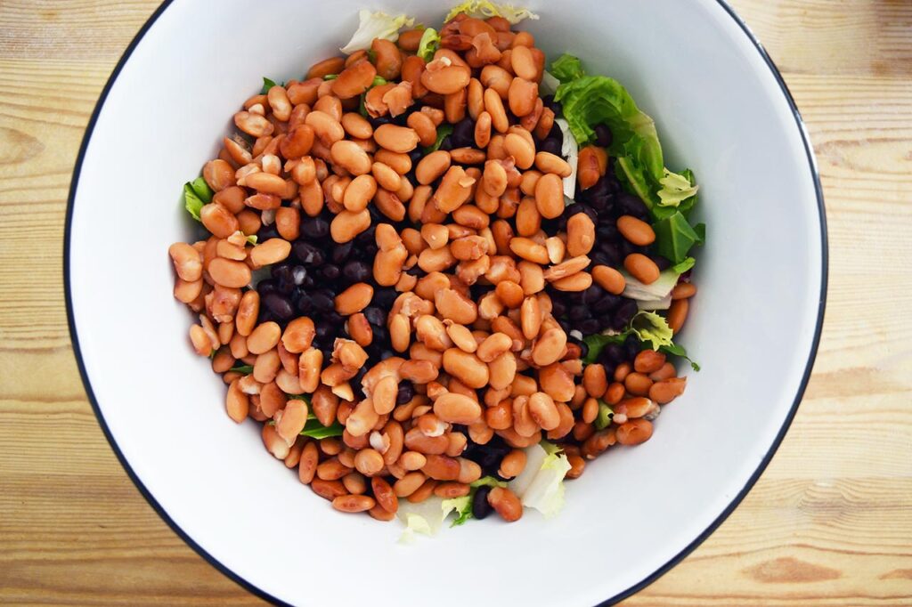 Beans layered over lettuce in a mixing bowl.