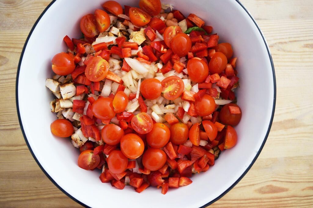 Halved cherry tomatoes added to a mixing bowl full of Mexican Dense Bean Salad ingredients.