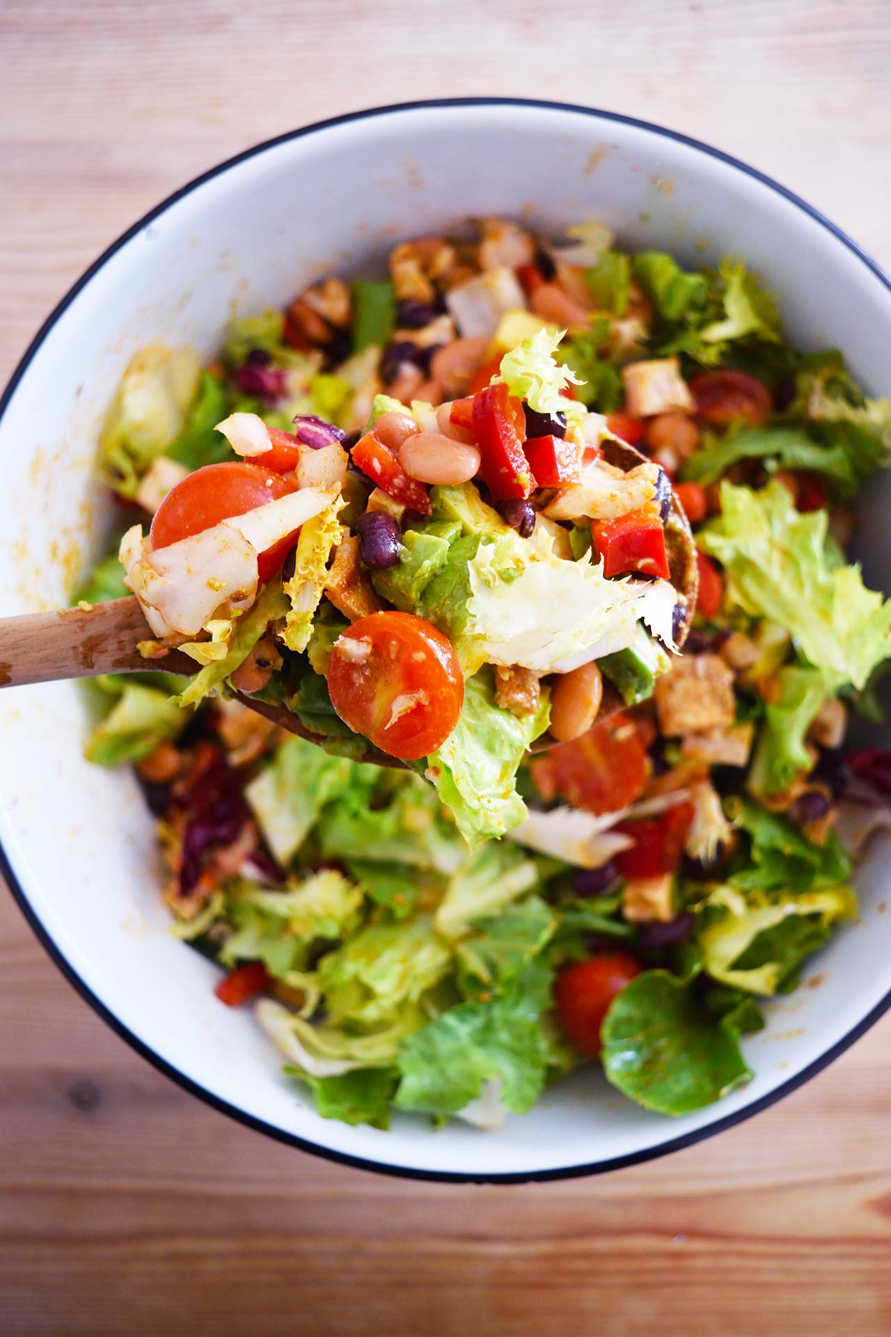 Overhead view of a wood spoon lifting up some Mexican Dense Bean Salad.