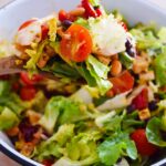 A wood spoon lifts up a spoonful of Mexican Dense Bean Salad from a bowl.