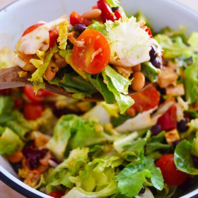 A wood spoon lifts up a spoonful of Mexican Dense Bean Salad from a bowl.