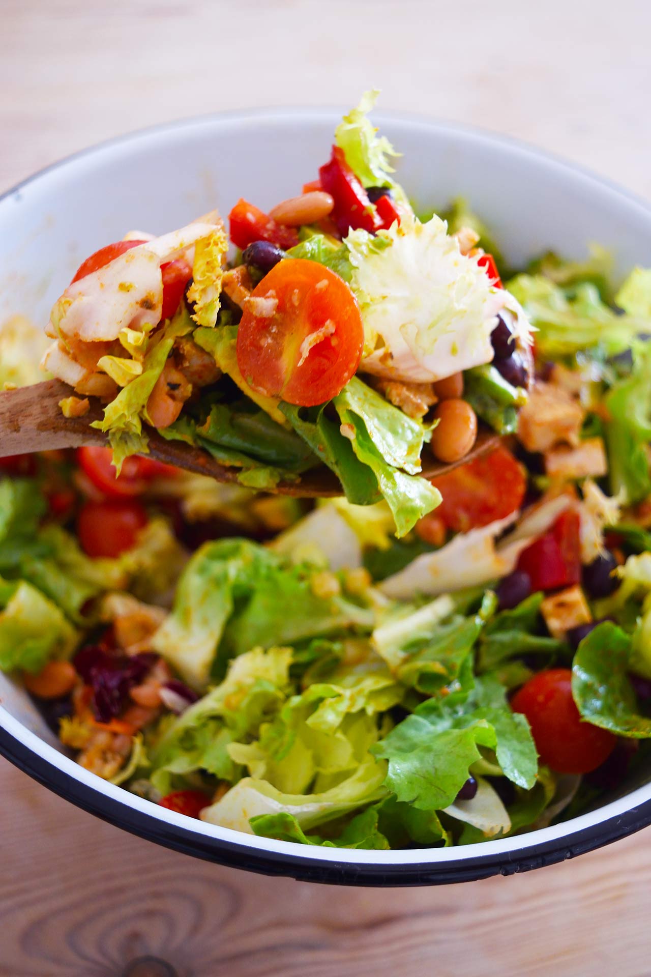 A wood spoon lifts up a spoonful of Mexican Dense Bean Salad from a bowl.