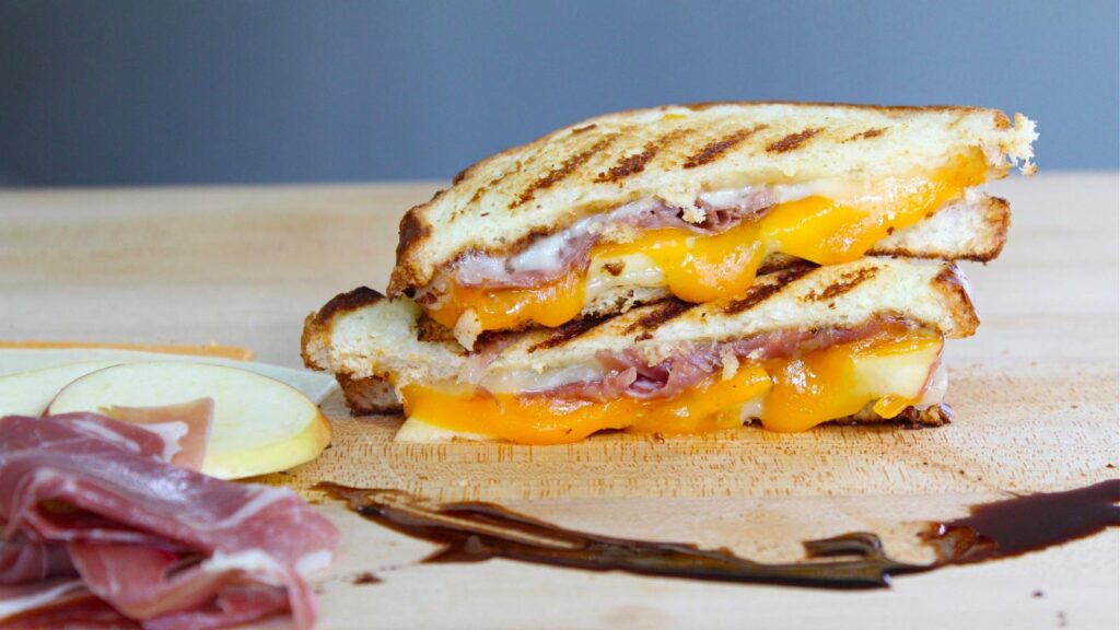 A cut and stacked prosciutto apple grilled cheese sandwich on a wood surface.