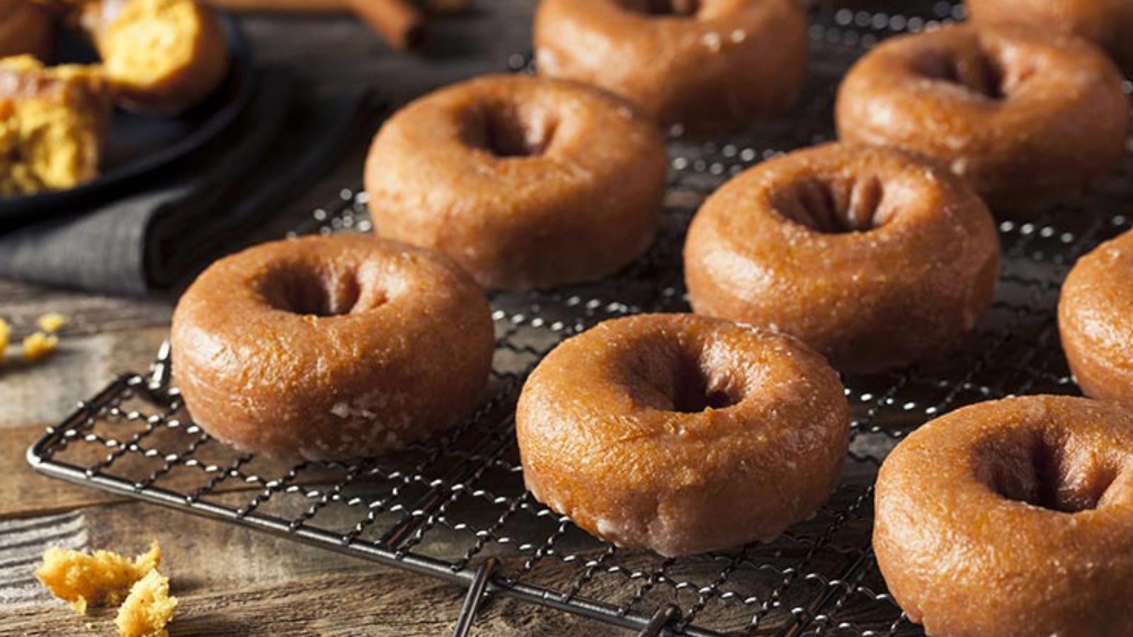Pumpkin donuts lined up on a wire cooling rack.