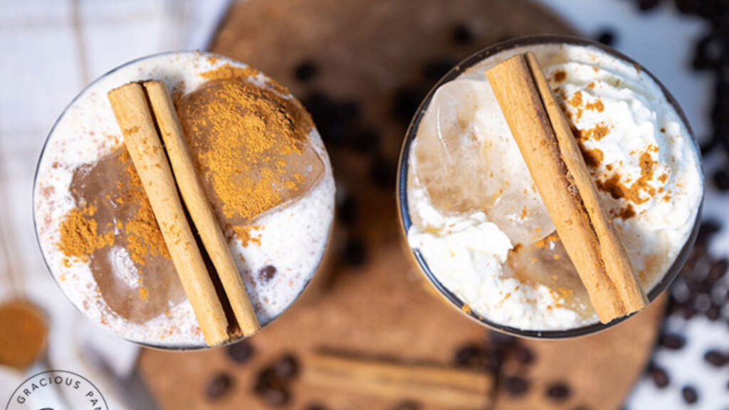 An overhead view of two glasses filled with pumpkin spice latte and topped with cinnamon sticks.