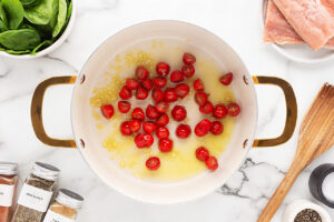 Halved cherry tomatoes added to a pot of oil and minced garlic.