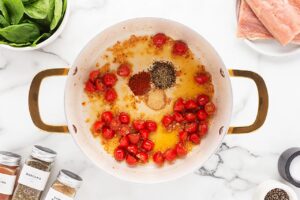 Spices added to a pot with oil, garlic and halved tomatoes in it.