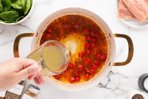 Adding stock to a pot of garlic and tomatoes.