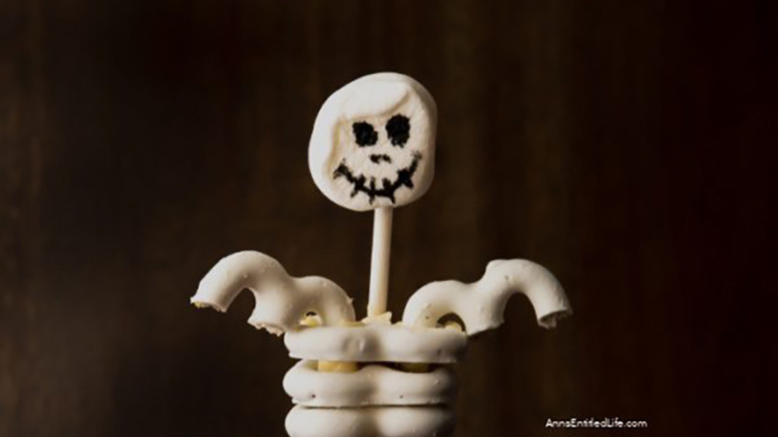 A skeleton cupcake topper on a dark, brown background.