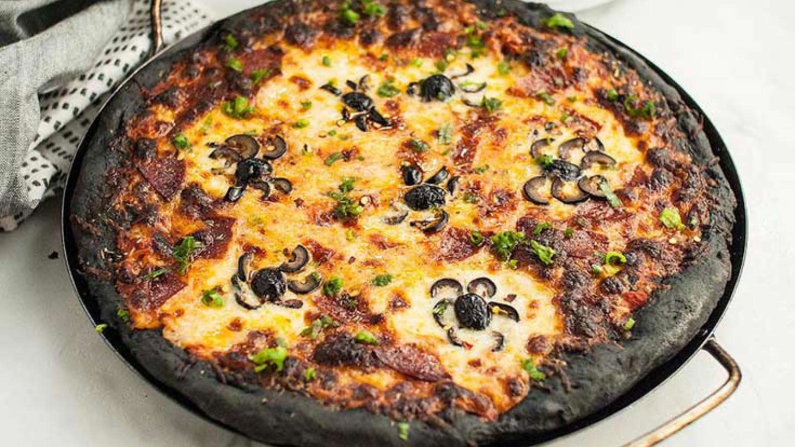 A pizza with black crust and black olive spiders on top.