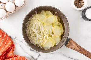 Sliced onions and potatoes in a skillet with oil.