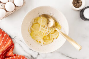 Cooled onions and potatoes in a white mixing bowl.
