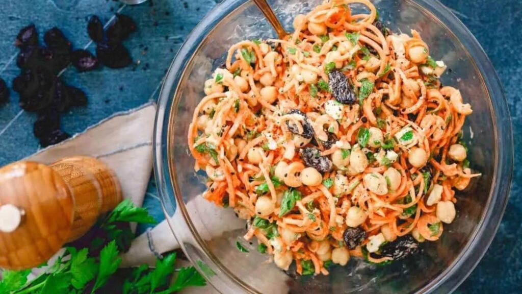 A spiralized carrot salad with chickpeas in a glass mixing bowl.