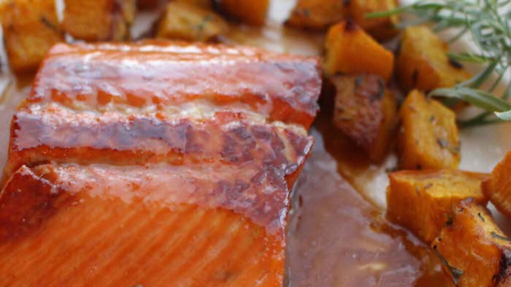 Closeup of a sweet bourbon salmon filet on a plate with roasted sweet potato chunks.