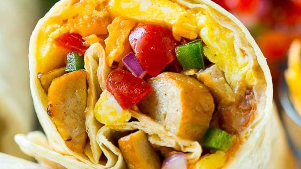 Closeup of a cut breakfast burrito showing eggs, sausage and veggies inside.
