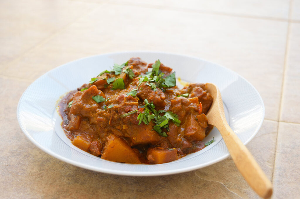 Side view of a bowl full of Butternut Squash Curry. A wood spoon rests on the right side of the bowl.