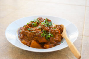 Side view of a bowl full of Butternut Squash Curry. A wood spoon rests on the right side of the bowl.