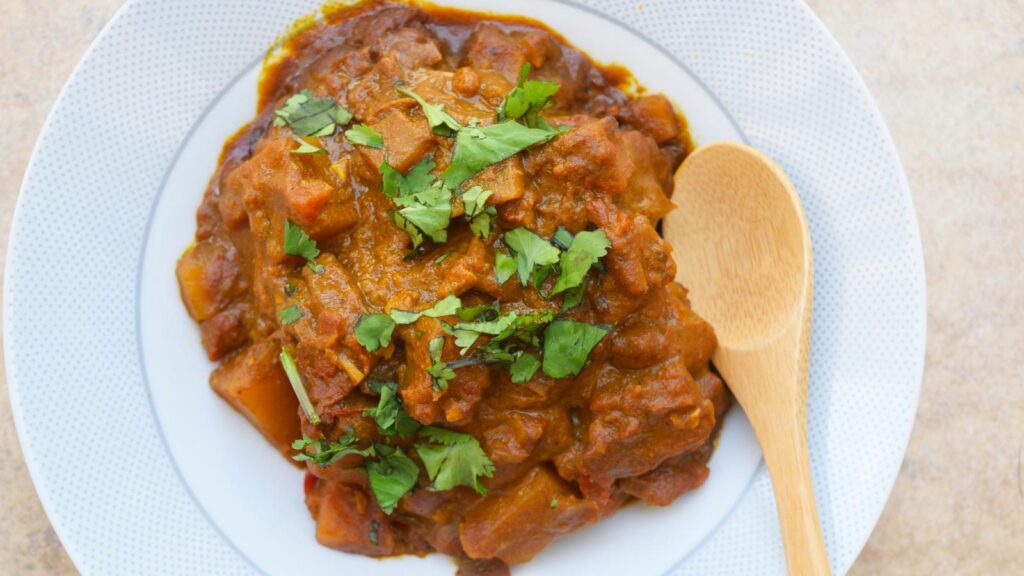 Overhead view of a white bowl filled with Butternut Squash Curry. A wood spoon rests to the side.