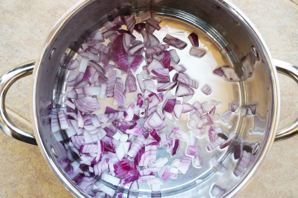 Chopped red onions in a pot with oil.