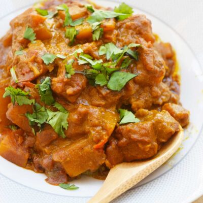 A closeup of a bowl full of Butternut Squash Curry with a wood spoon resting on the side of the bowl.